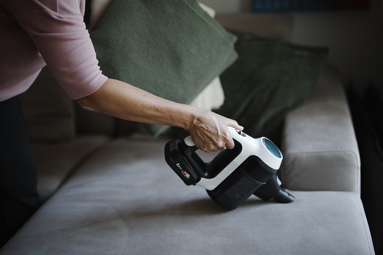 Handheld vacuum cleaning a sofa cushion in a living room