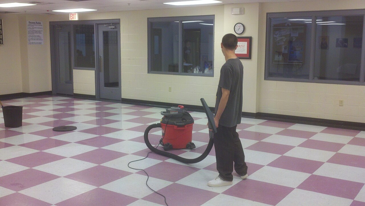 Cleaner vacuuming a large checkered-floor hall in a commercial building
