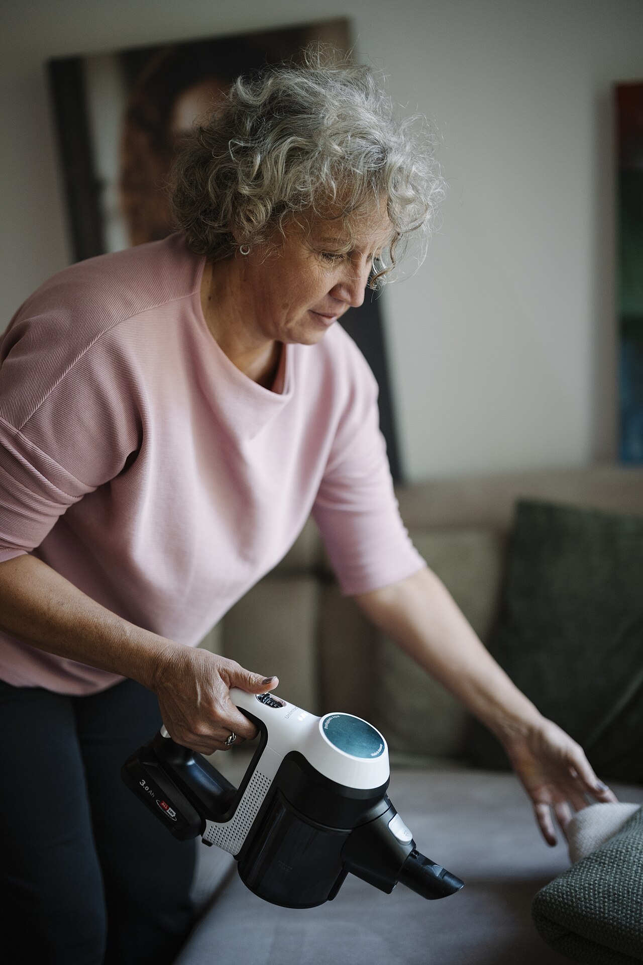 Cleaner using a handheld vacuum on a sofa in a bright living room
