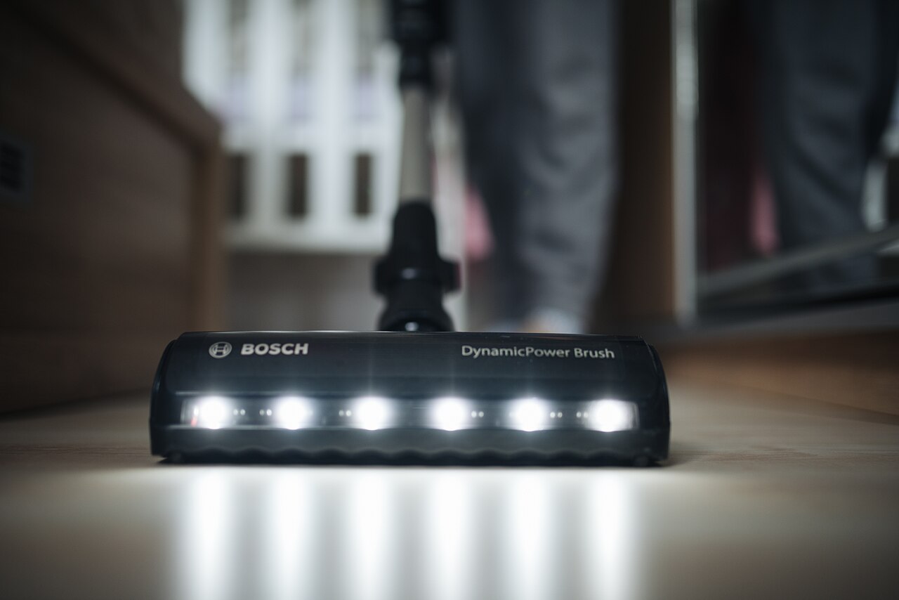 Vacuum cleaner head with lights cleaning a hard floor indoors